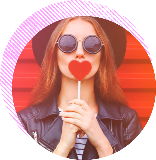 A woman holds a heart shaped lollipop in front of her mouth
